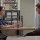 A woman and a man sit across from each other at a table in a well-lit restaurant.